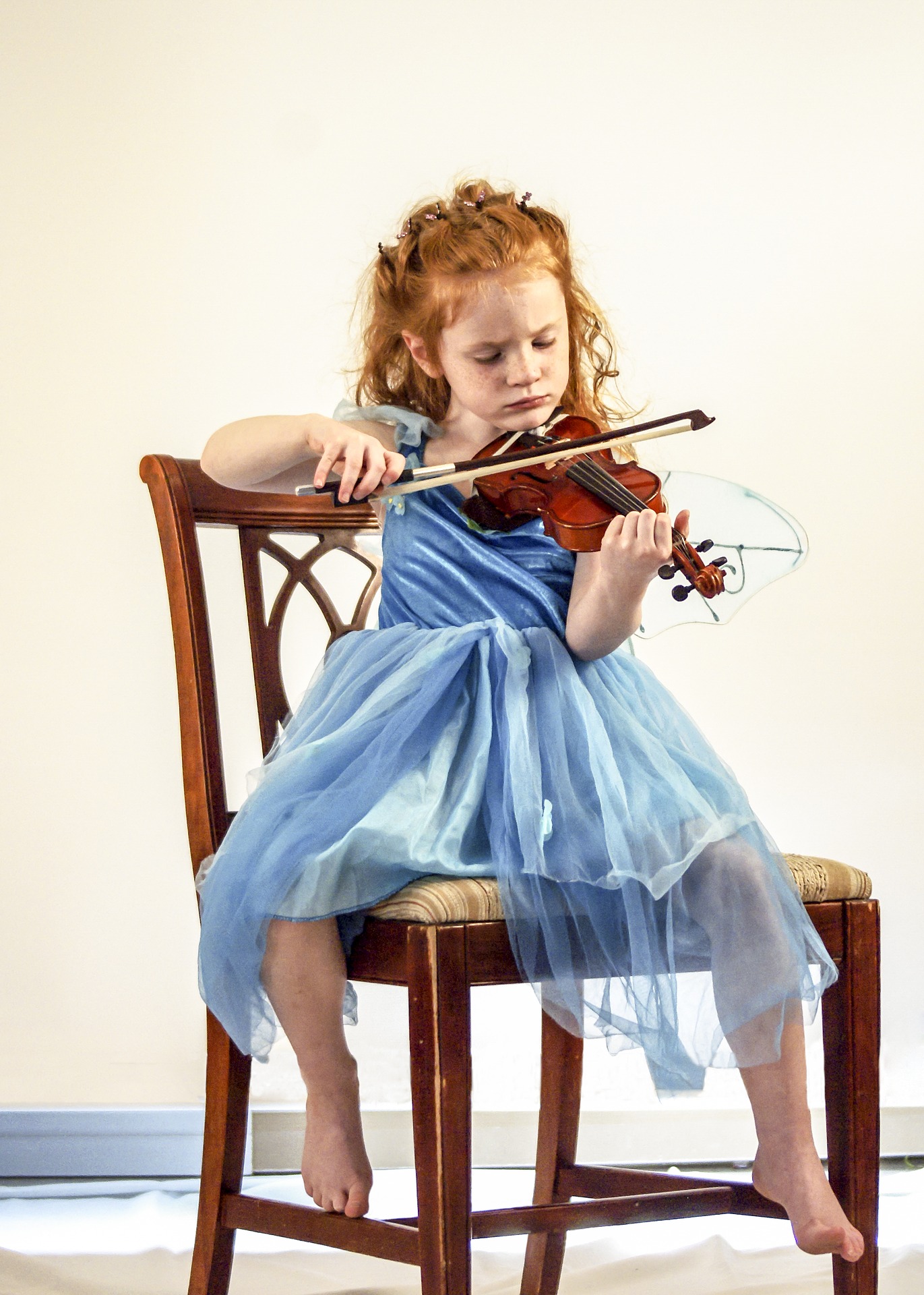 Zdjęcie przedstawia małą dziewczynkę grającą na skrzypcach