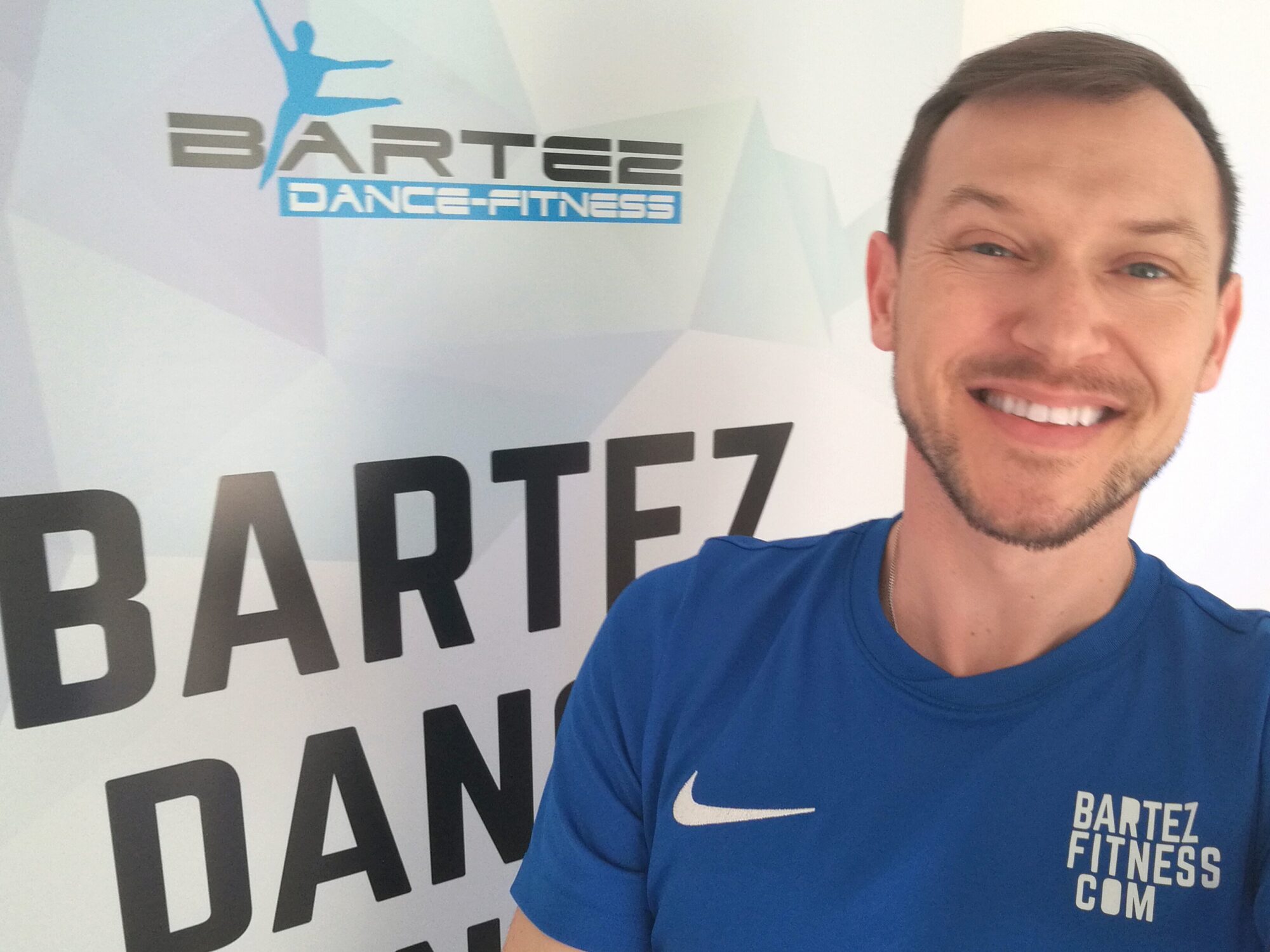Uśmiechnięta twarz mężczyzny na tle jasnego tła z napisem Bartez Dance